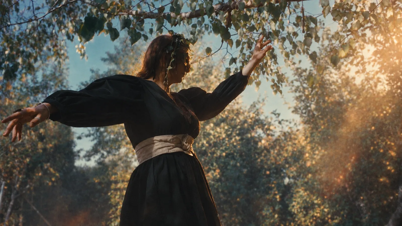 Hilbi danse sous les bouleaux, les bras ouverts, dans la lumière du soir